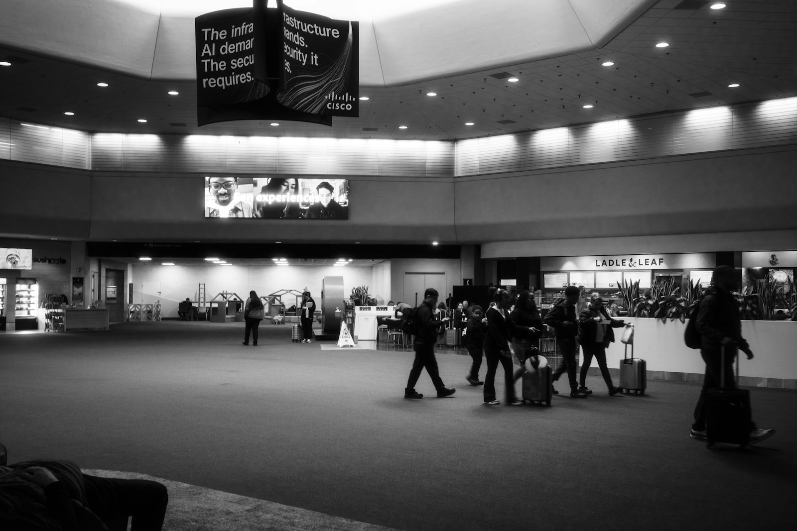 Black and white view of travelers and luggage in a large airport terminal.