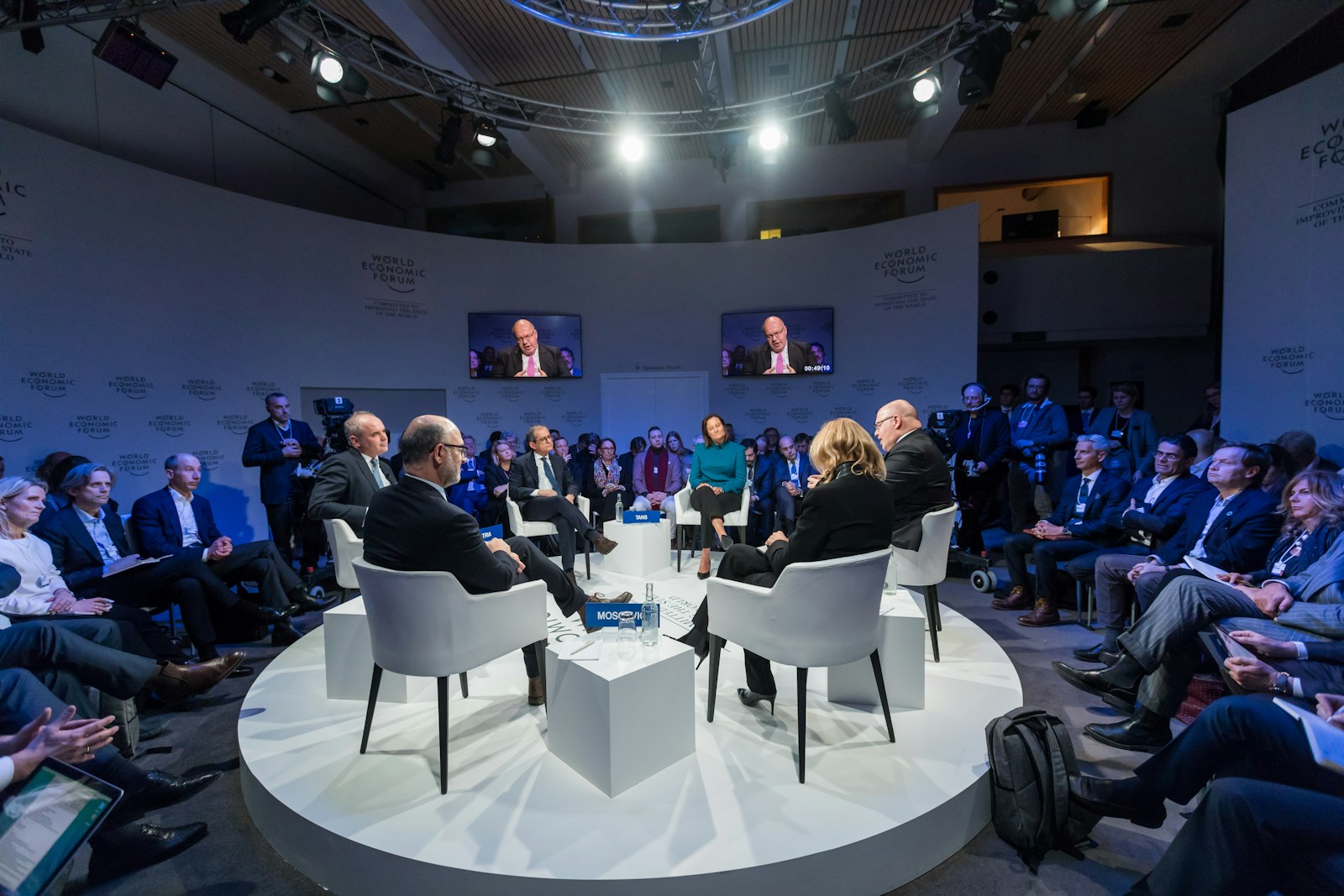 Panelists seated in a circle with an audience at an indoor conference.