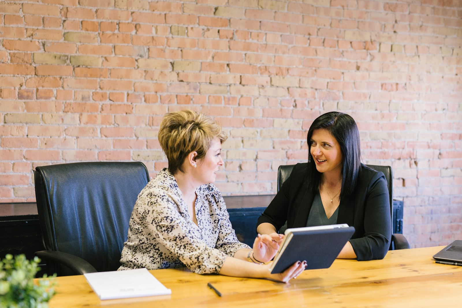 Two professionals reviewing a tablet across a meeting table.
