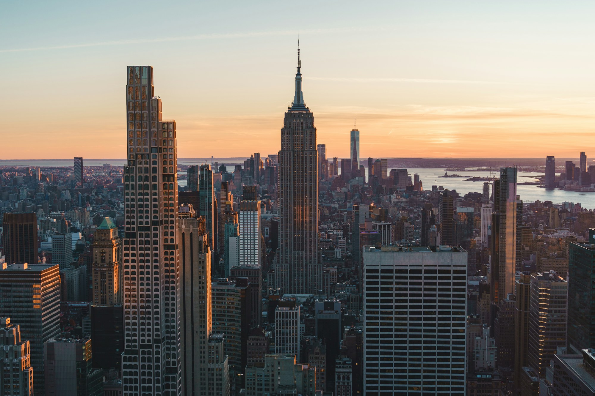 Manhattan skyscrapers and the Empire State Building at sunset, with the river in the distance.